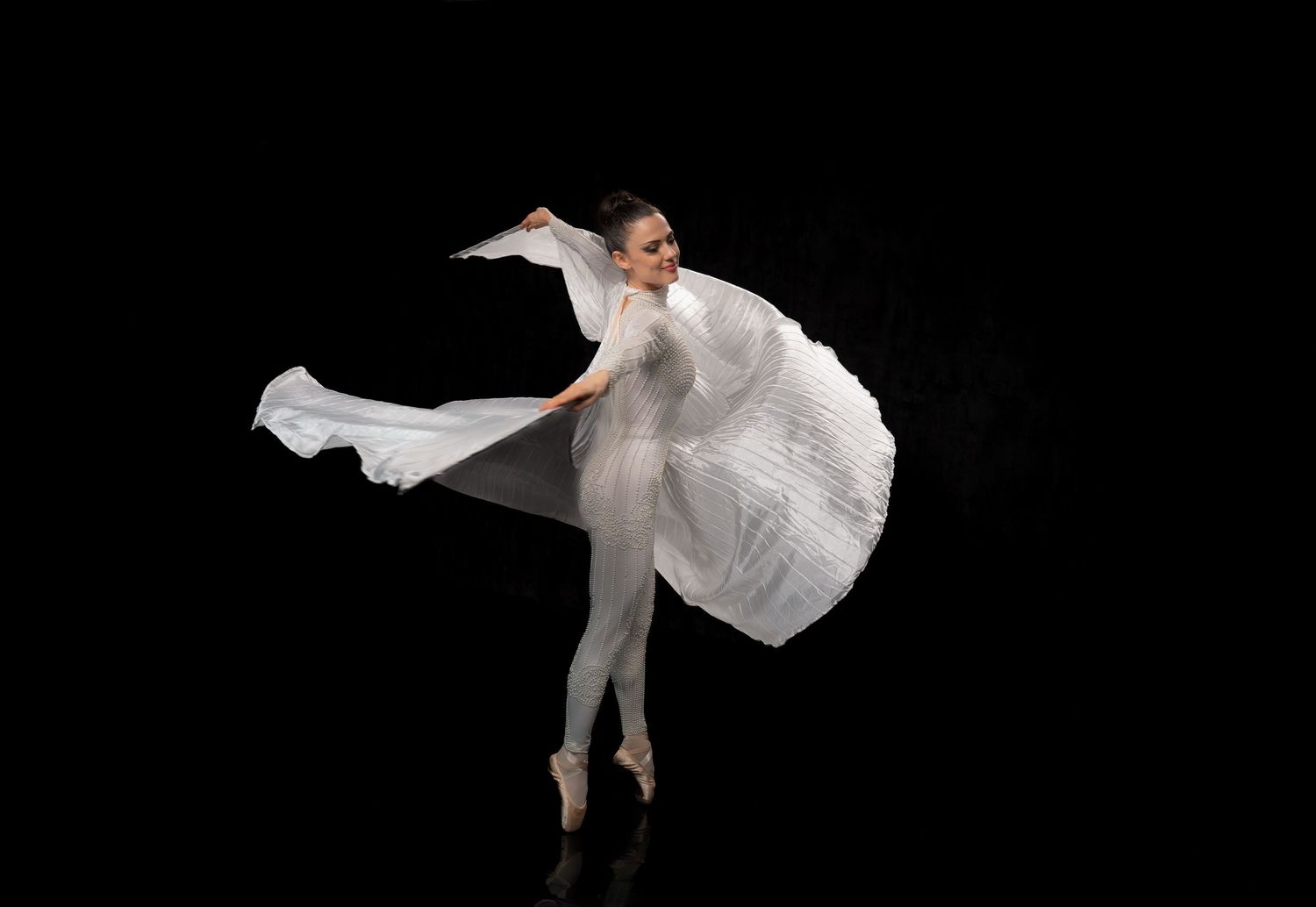 Dancer in flowing white dress performing against black background.