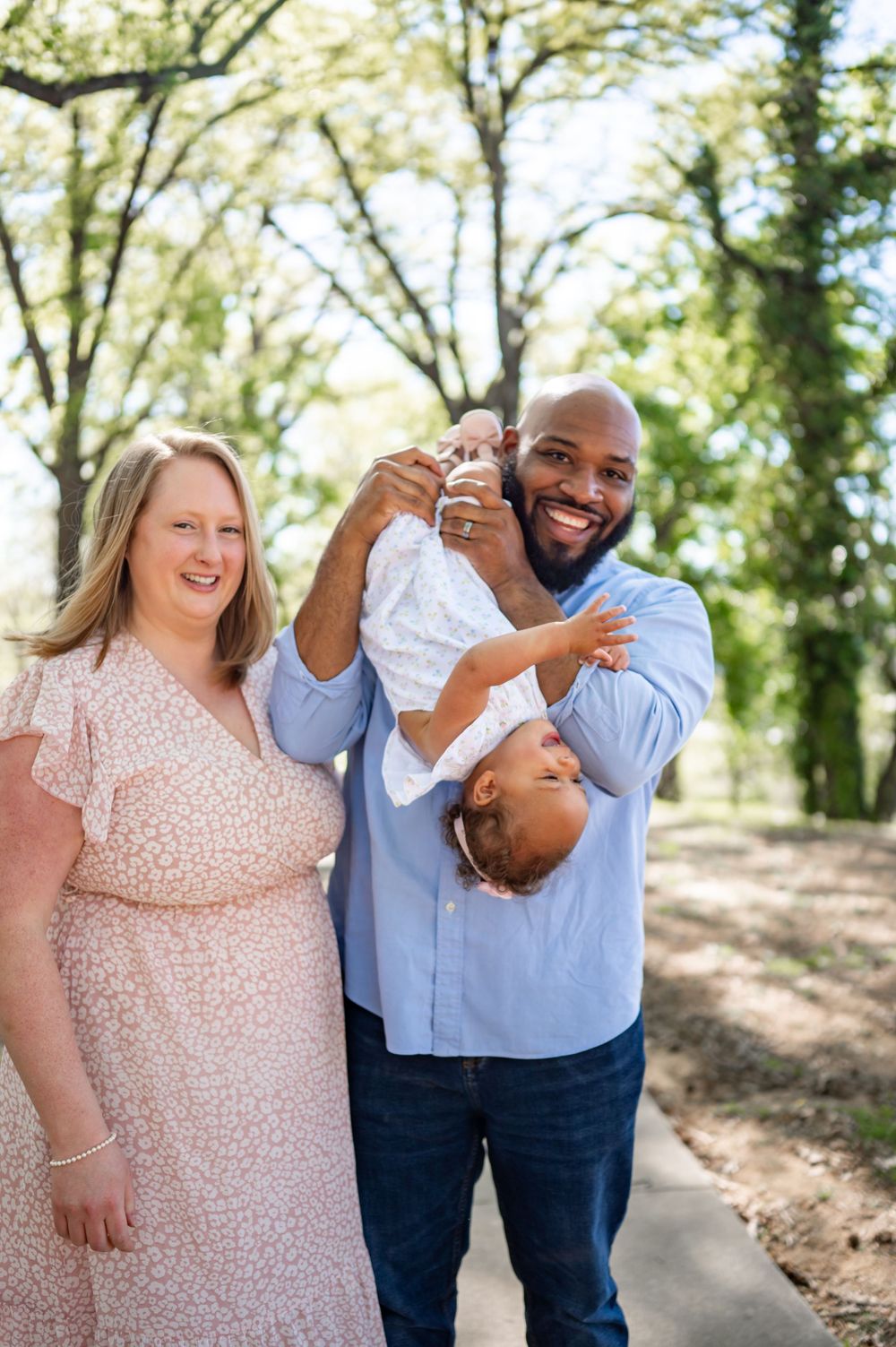 Playful family moment outdoors with parents in casual attire holding their child.