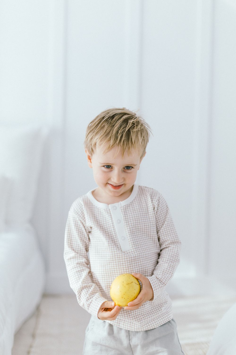 Child in white sweater holding yellow fruit against white background.