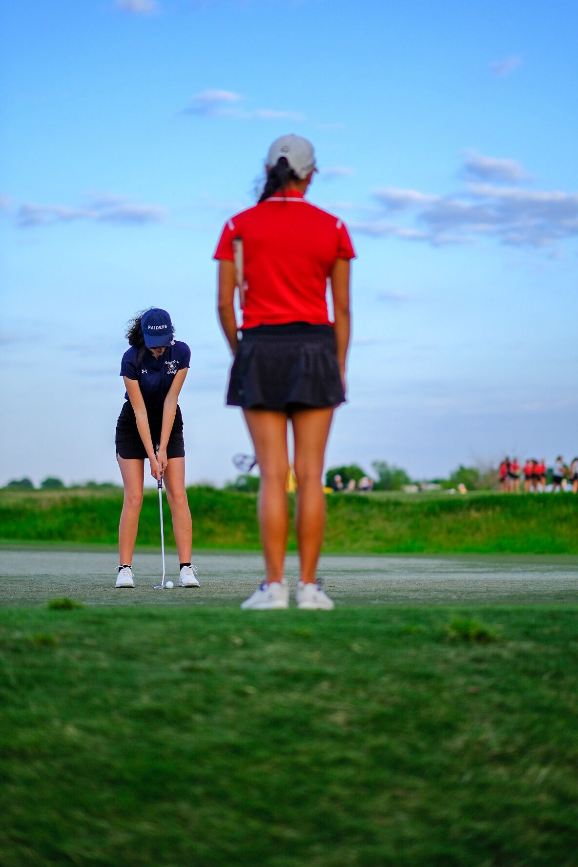 Young woman on her final putt while young lady in red shirt waits patiently.