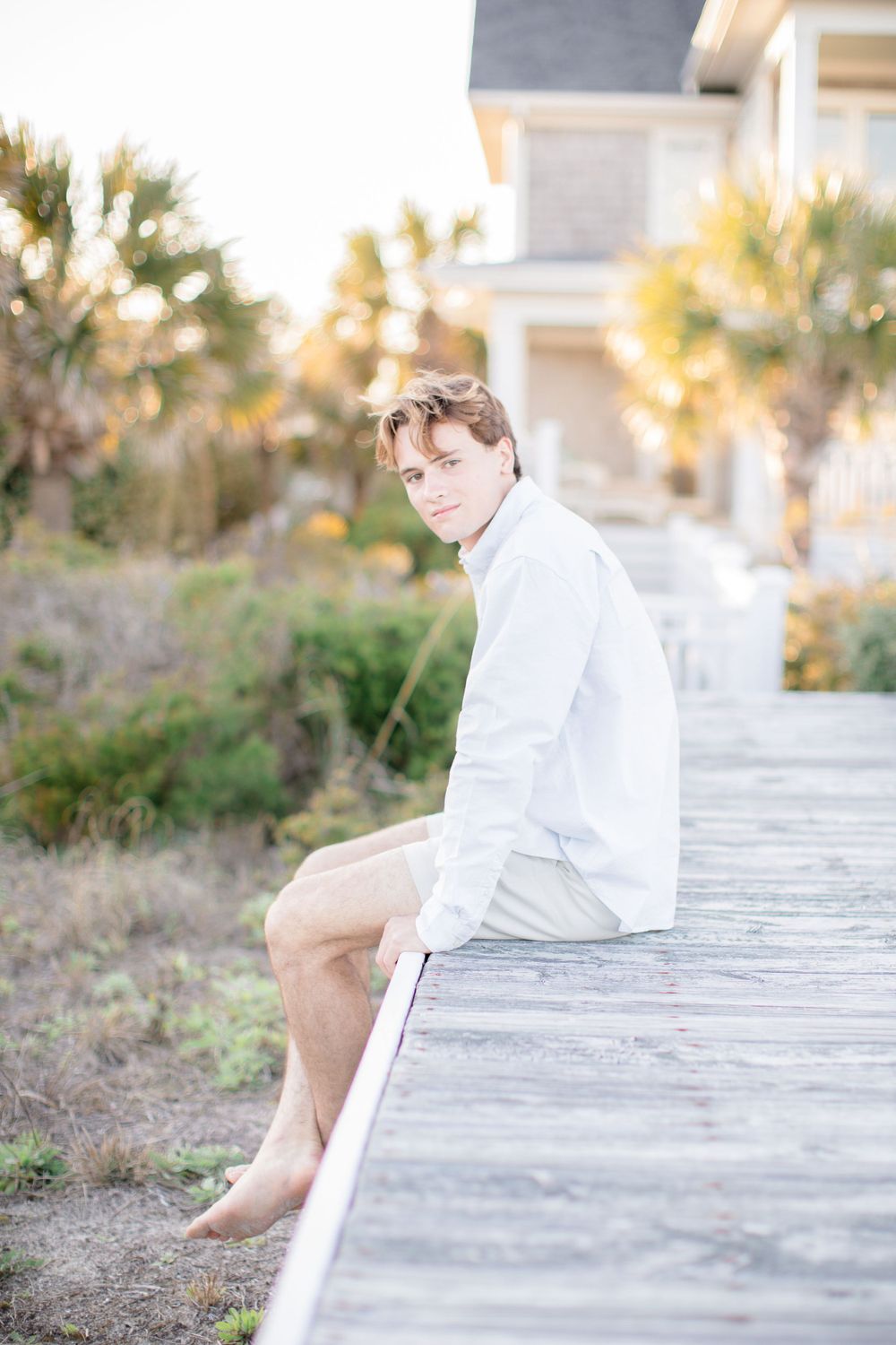 Casual portrait of someone sitting on wooden boardwalk with coastal home in background.