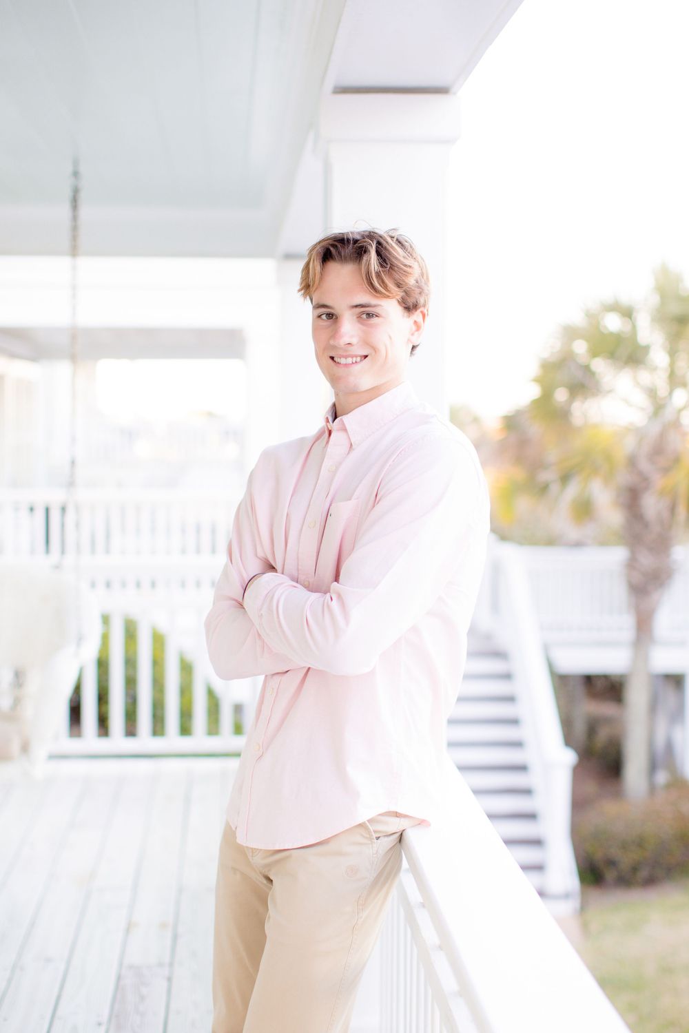 Portrait of someone in pink shirt standing on white porch with arms crossed.