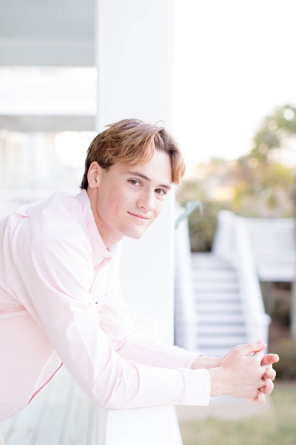 Person in pink dress shirt leaning against white railing on a bright sunny day.