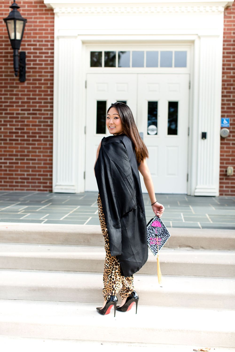 Stylish outfit featuring leopard print pants and black coat in front of grand white entrance.