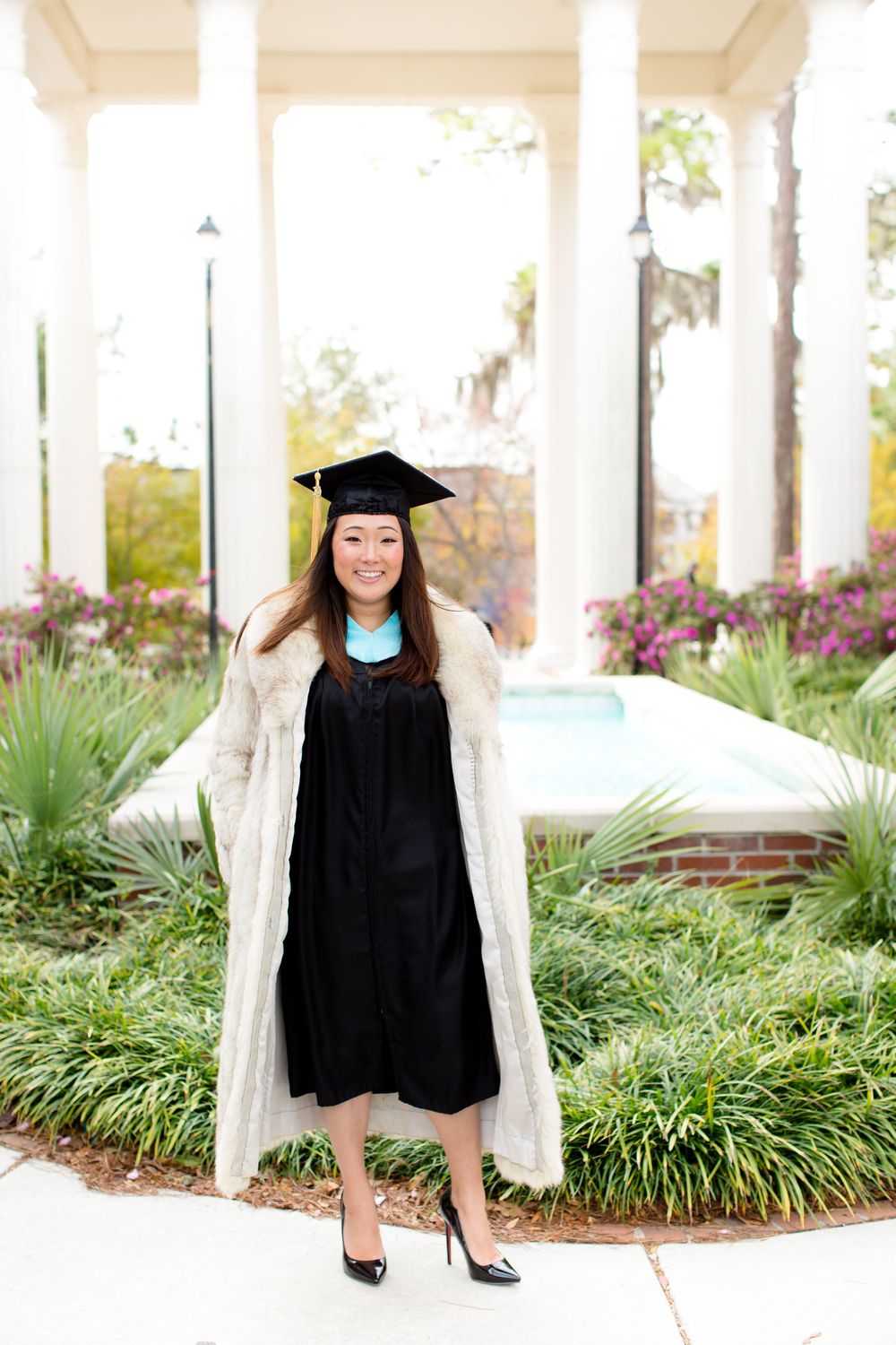 Graduate in black gown and white coat poses in front of columned structure.