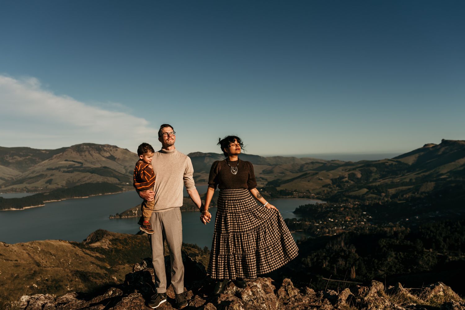 A family stands together against a scenic mountain backdrop overlooking a serene lake landscape.
