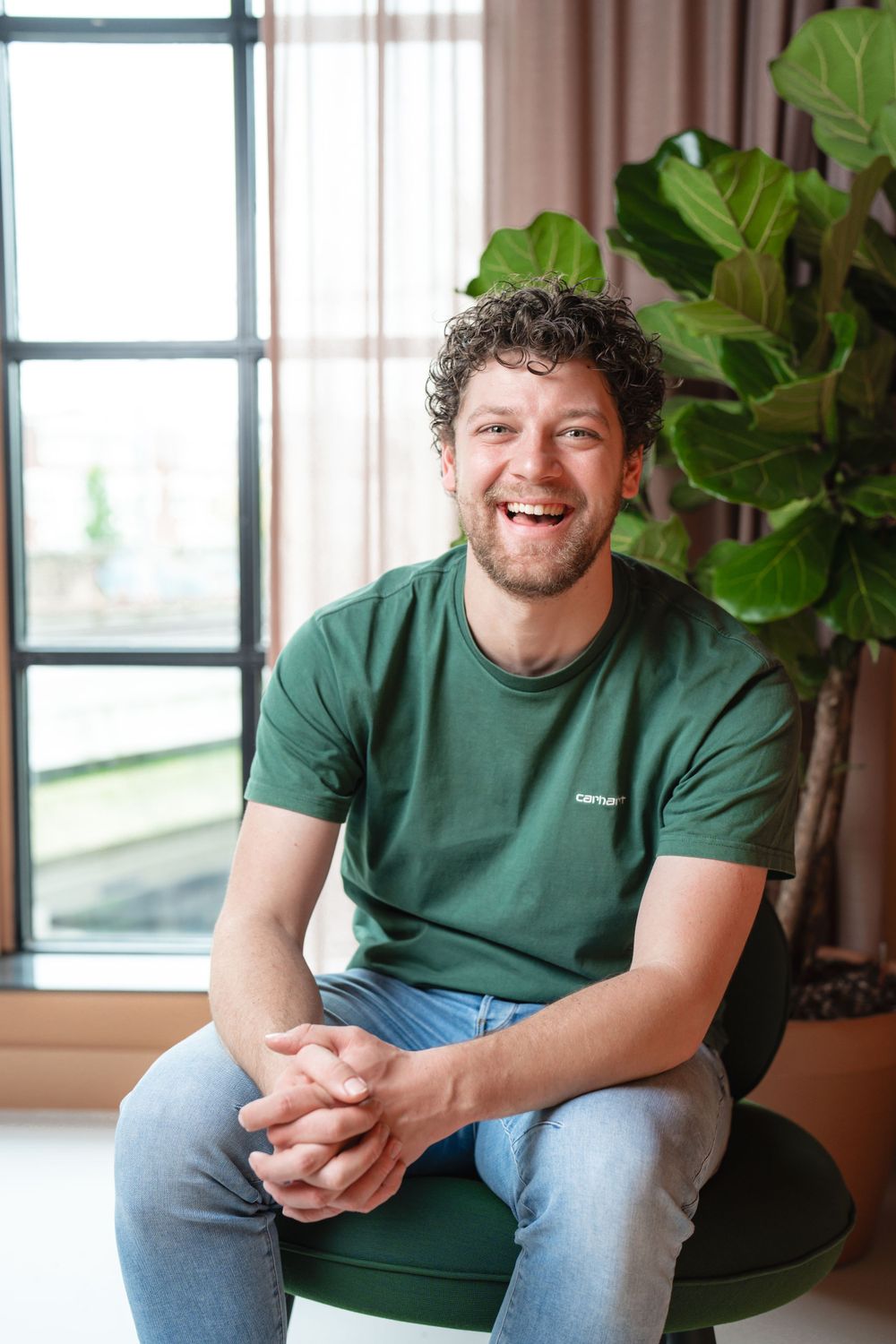 Casual professional seated on green chair next to large indoor plant.