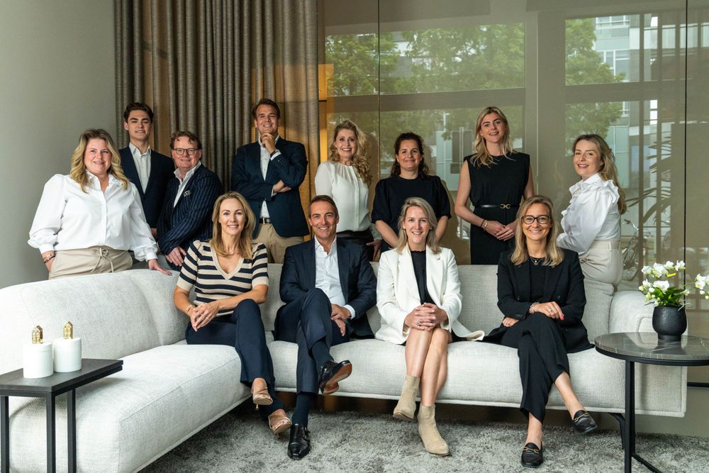 Professional team members pose together on a white couch in an elegant living room setting.