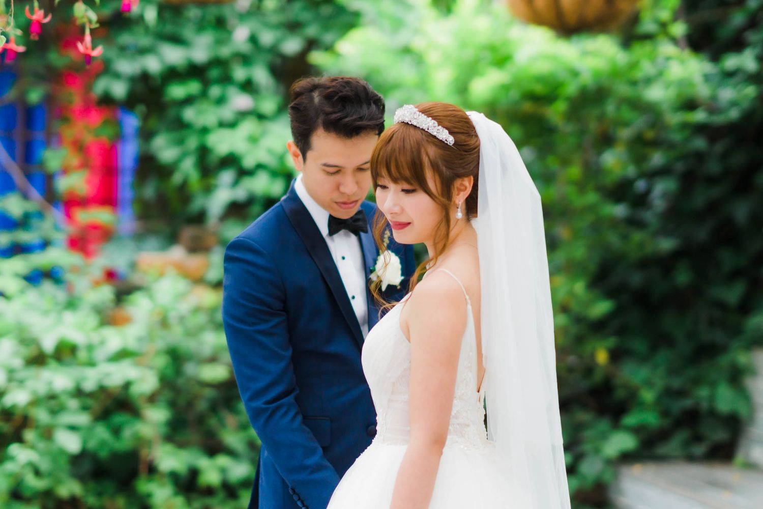A romantic wedding portrait with a couple in formal attire against lush green garden backdrop.