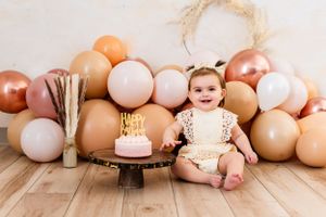 Festive scene with baby surrounded by peachy pink balloons and rustic decorations.