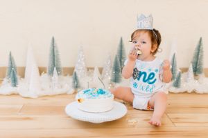 Baby cake smash photo session with blue and white winter decorations on wooden floor.