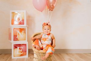 First birthday celebration setup with pink balloons and decorative frames against white wall.