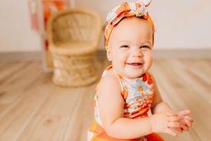 Happy baby in orange outfit crawling during birthday photoshoot with white backdrop.