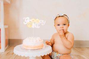 Birthday cake with glowing candle and festive decorations for baby's first birthday celebration.