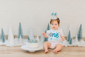 Baby in blue dress surrounded by silver winter-themed decorations.