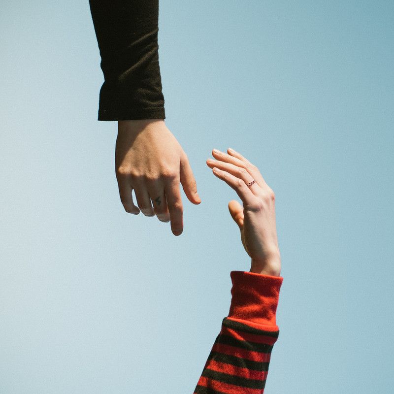 A photograph of two hands reaching for each other from the top and bottom, the blue sky in the background