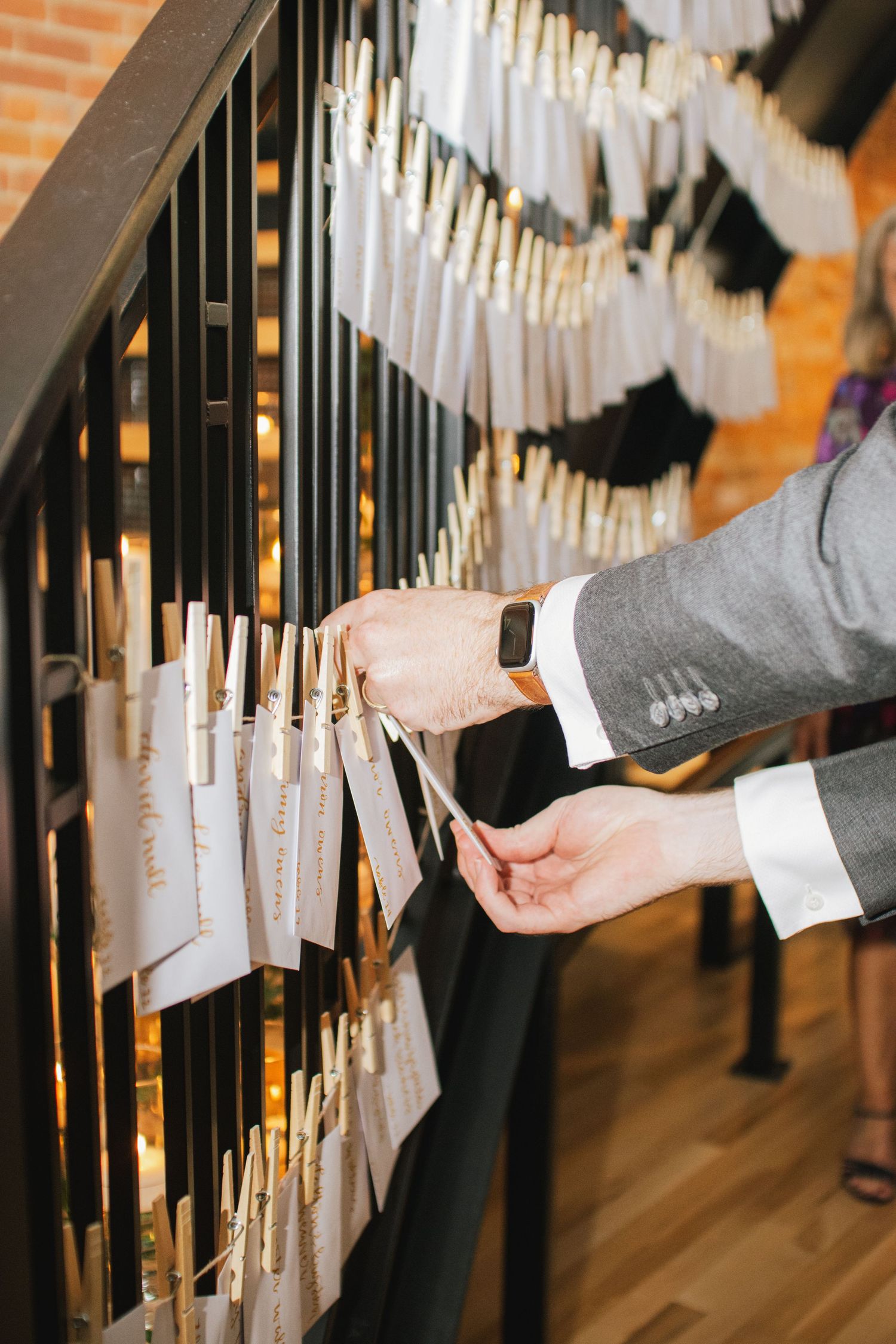 Wedding guests reaching for escort cards displayed on elegant black railings with white tassels.
