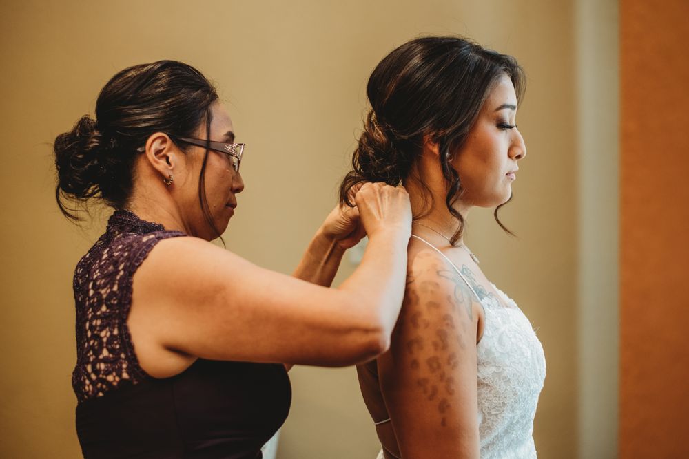 Helper assisting with dress preparations during wedding day.