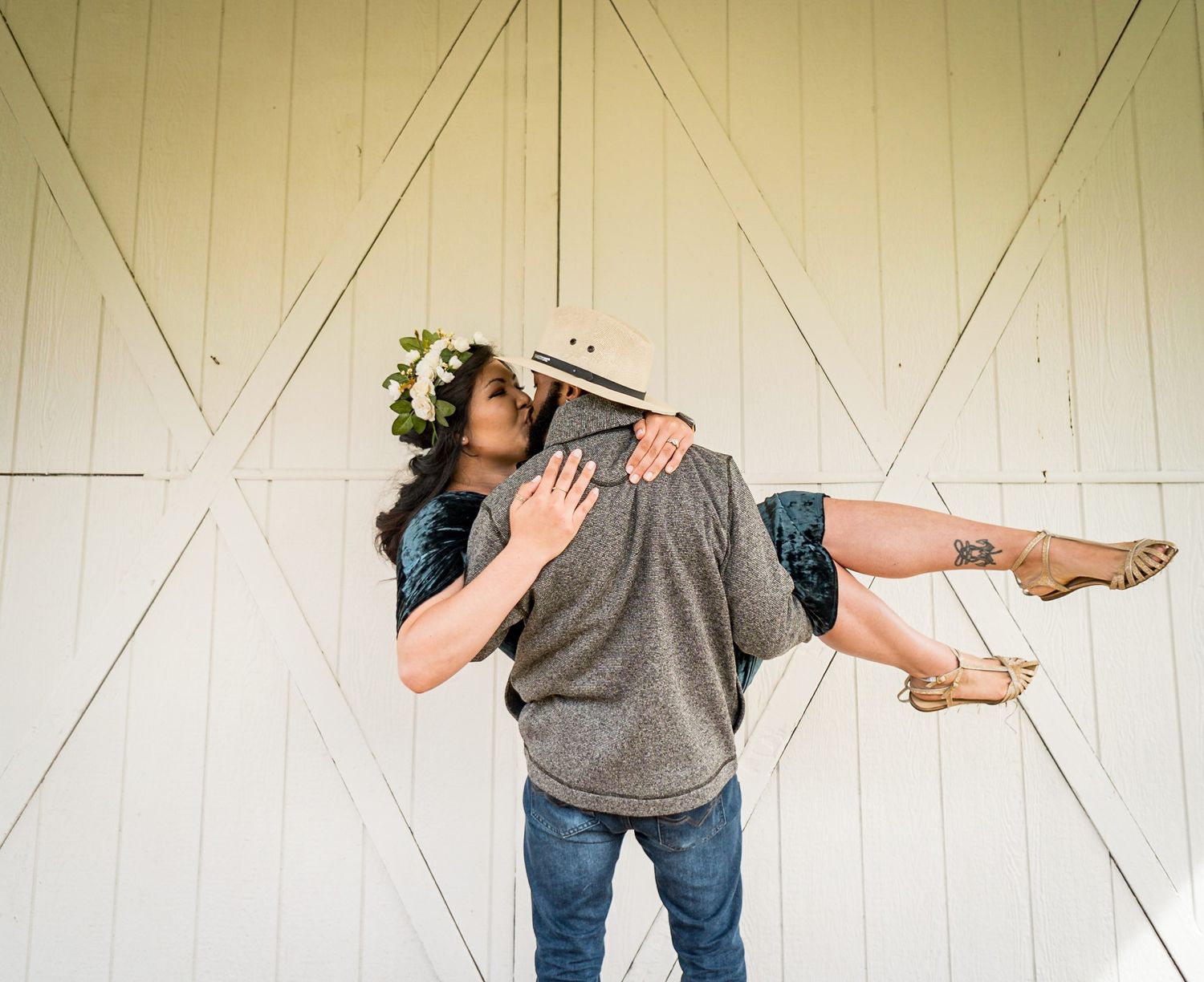 Romantic couple posing playfully against white barn doors.