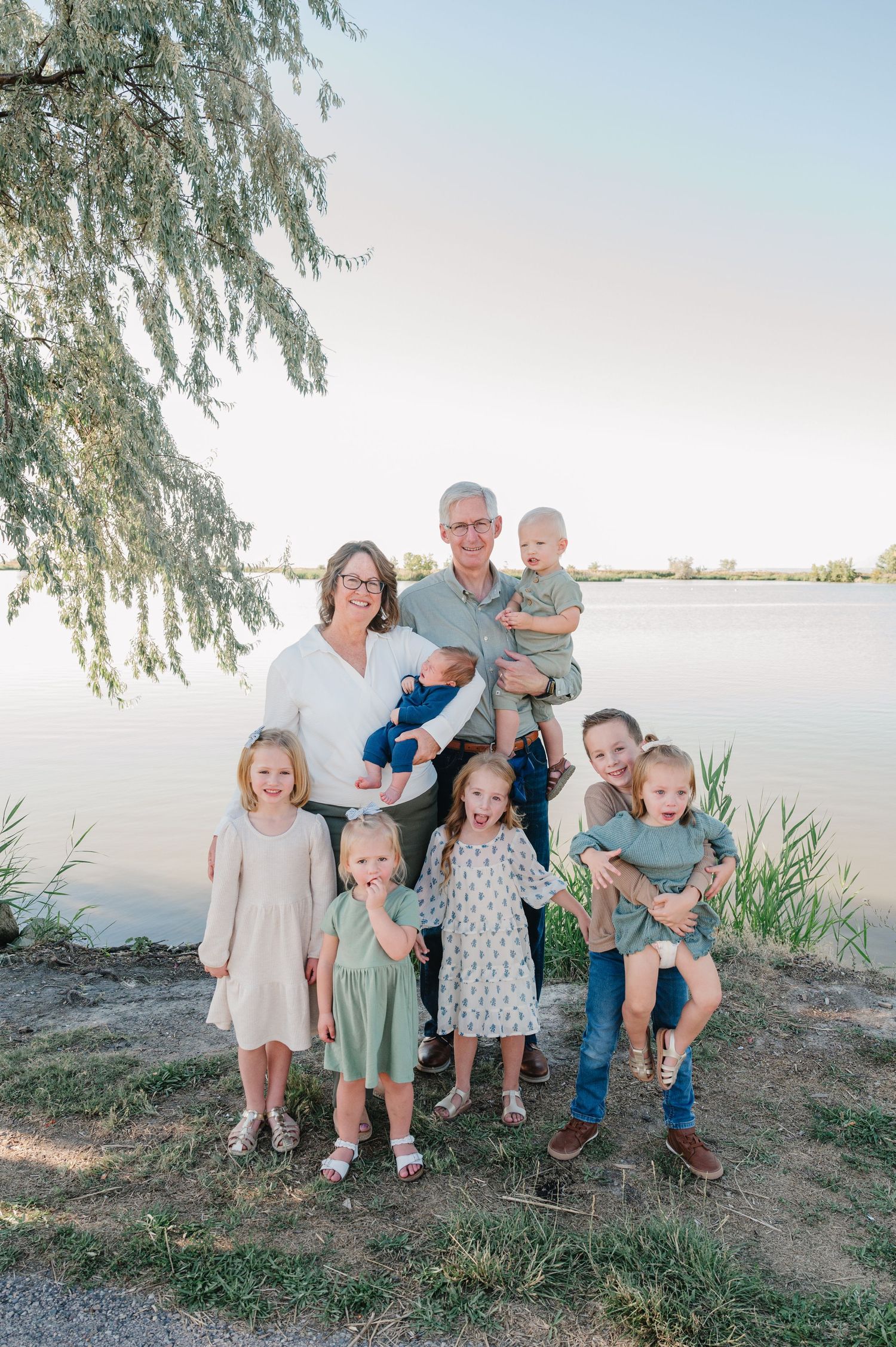 Family group portrait by a lake with willow trees in soft evening light.