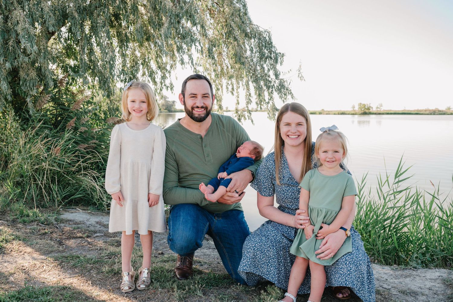 Family portrait by a lakeside with willow trees and natural lighting.