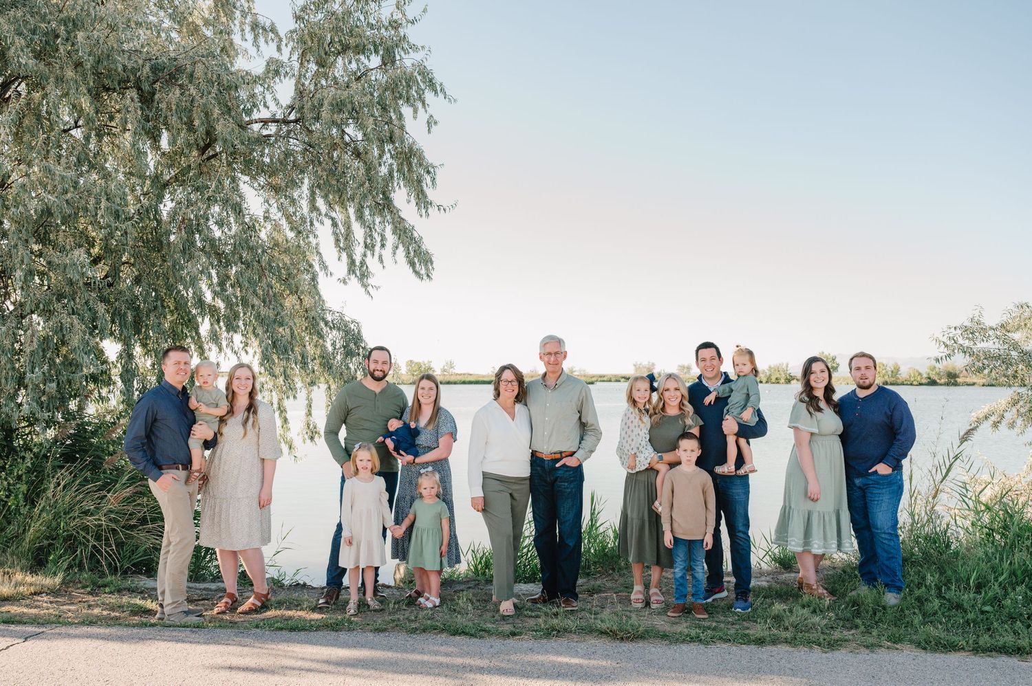 Large extended family group poses together by lake under willow tree branches.