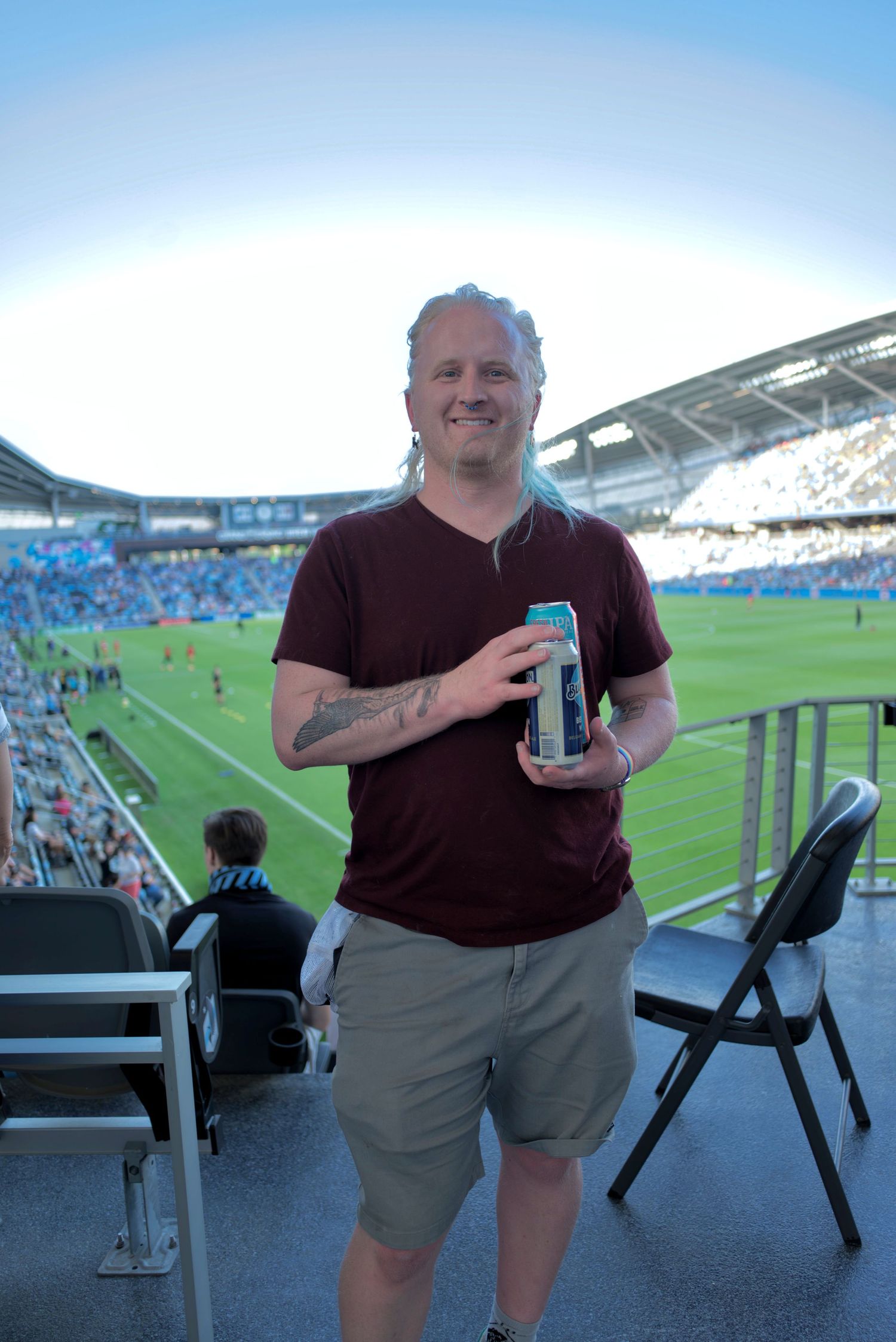 Smiling man with gray hair holding energy drink can at outdoor soccer stadium event.
