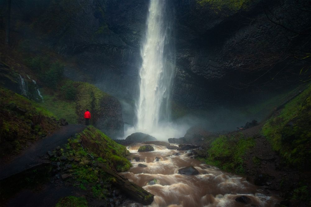 Dramatic waterfall tumbling down rocky cliffs surrounded by green vegetation in misty conditions.