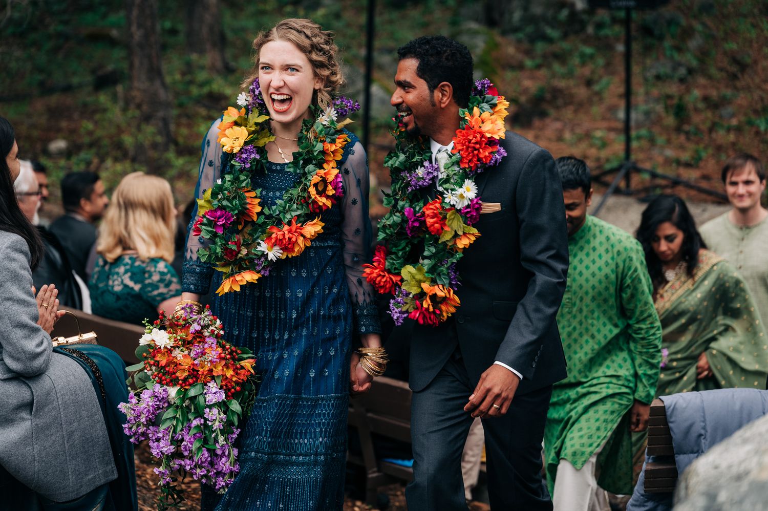 Wedding couple wearing colorful Hawaiian leis laugh during outdoor ceremony.