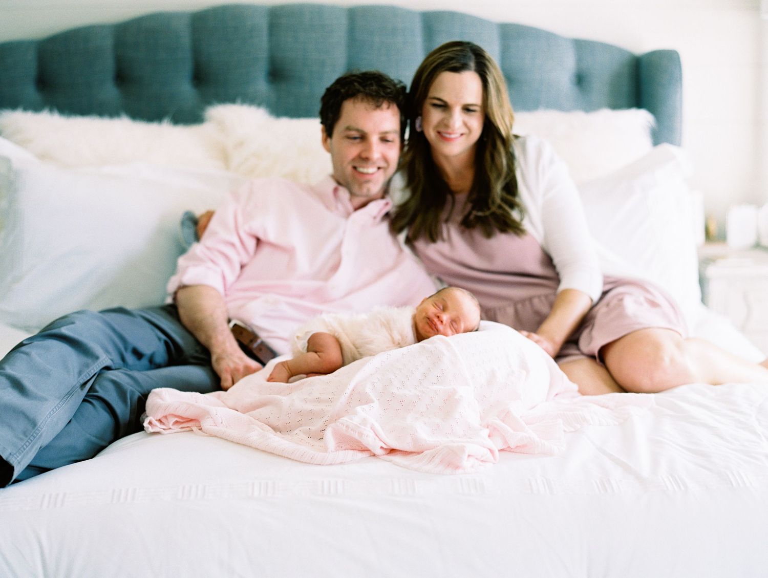 Couple relaxing together on a tufted headboard bed with white bedding and pillows.