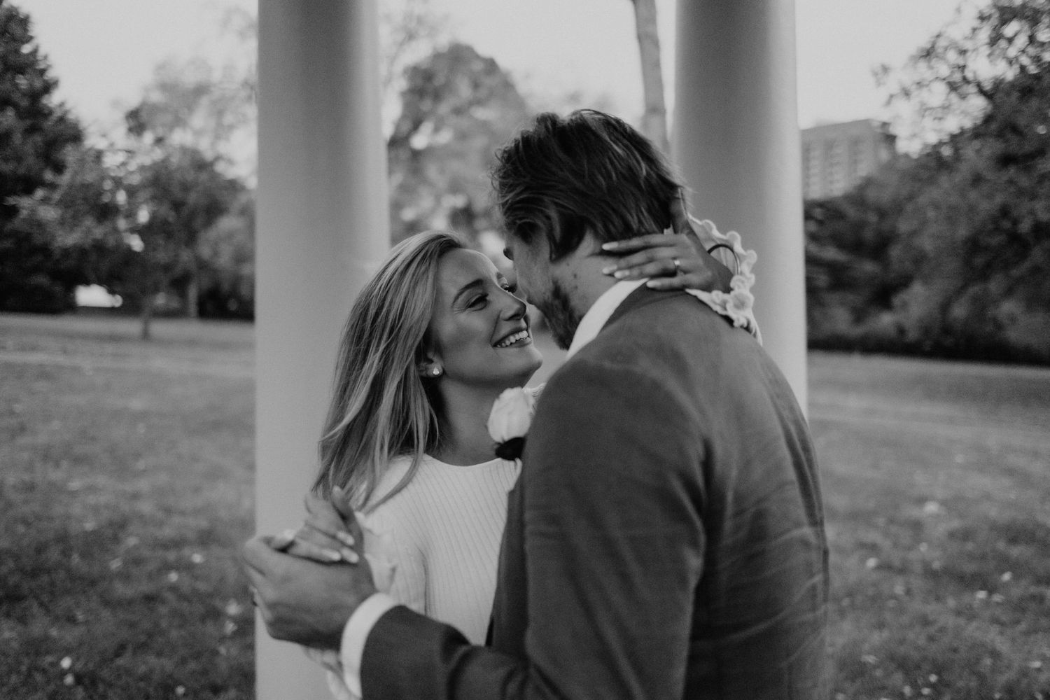 Elegant couple embracing under classical white columns in a garden setting.