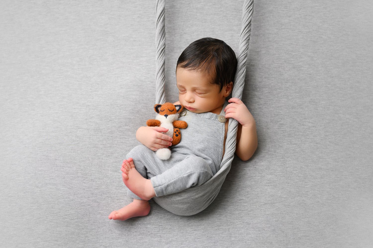 Newborn baby lying on soft gray backdrop in minimalist photography style.
