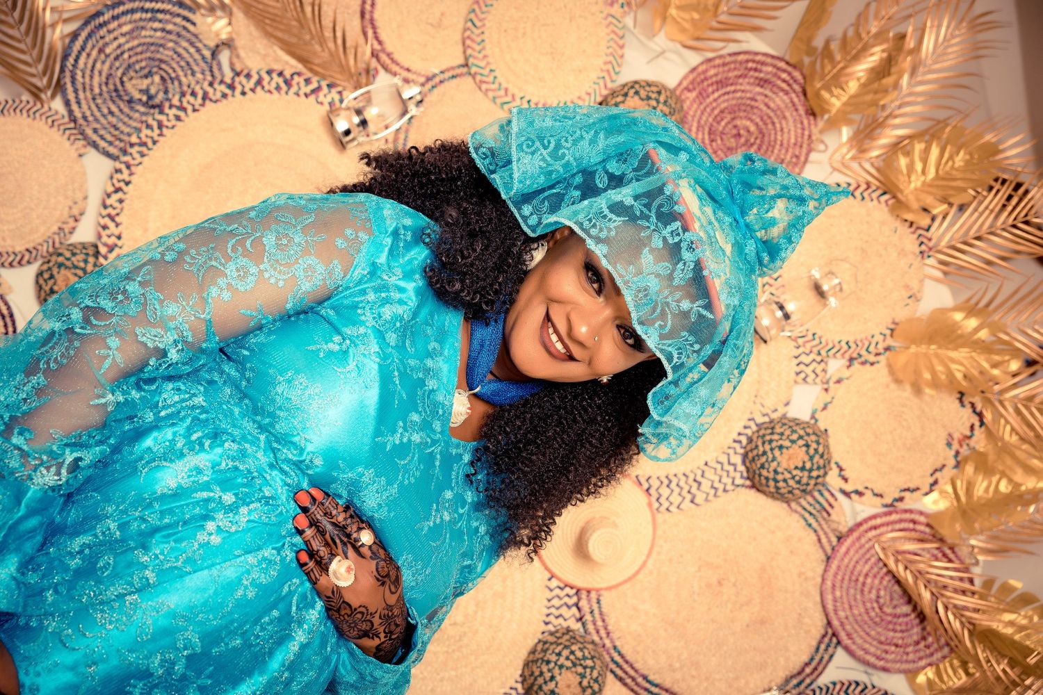 A joyful person in a turquoise traditional dress lying on patterned fabric.