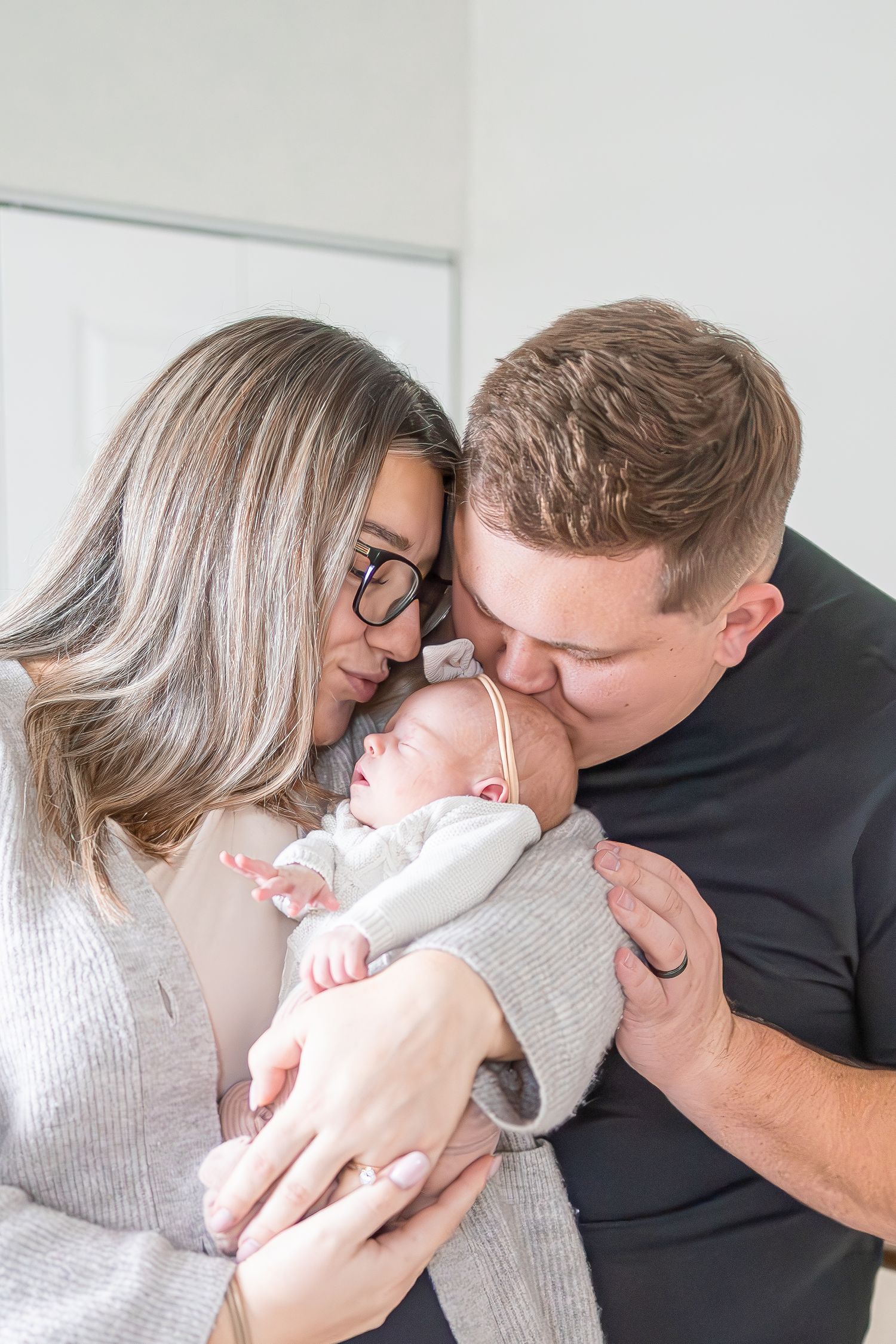 Parents share an intimate moment with their sleeping newborn baby against a white background.