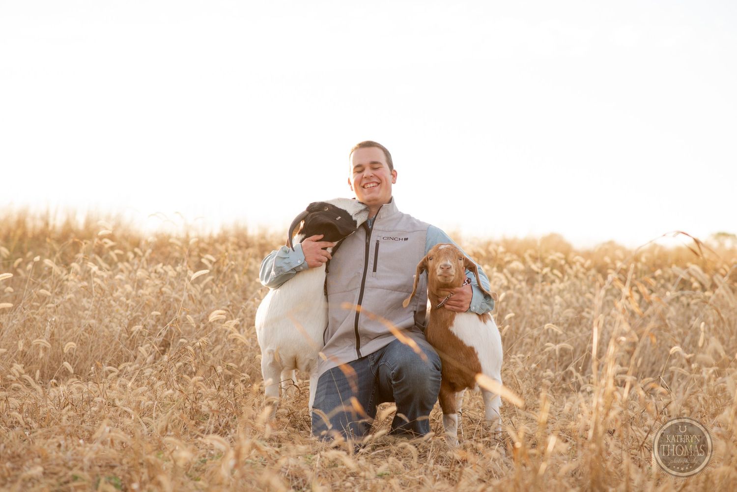 Person kneeling with two friendly dogs in a sunlit field of tall grass.