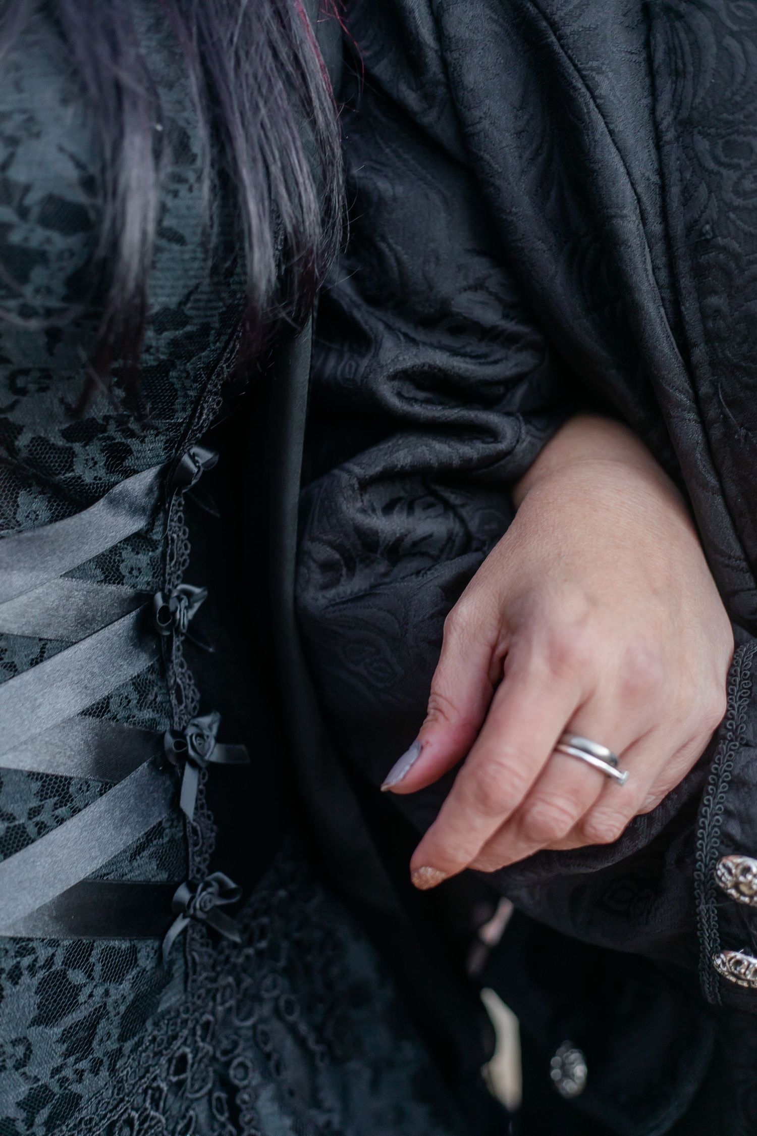 A hand wearing a wedding ring rests against black gothic-style dress fabric.