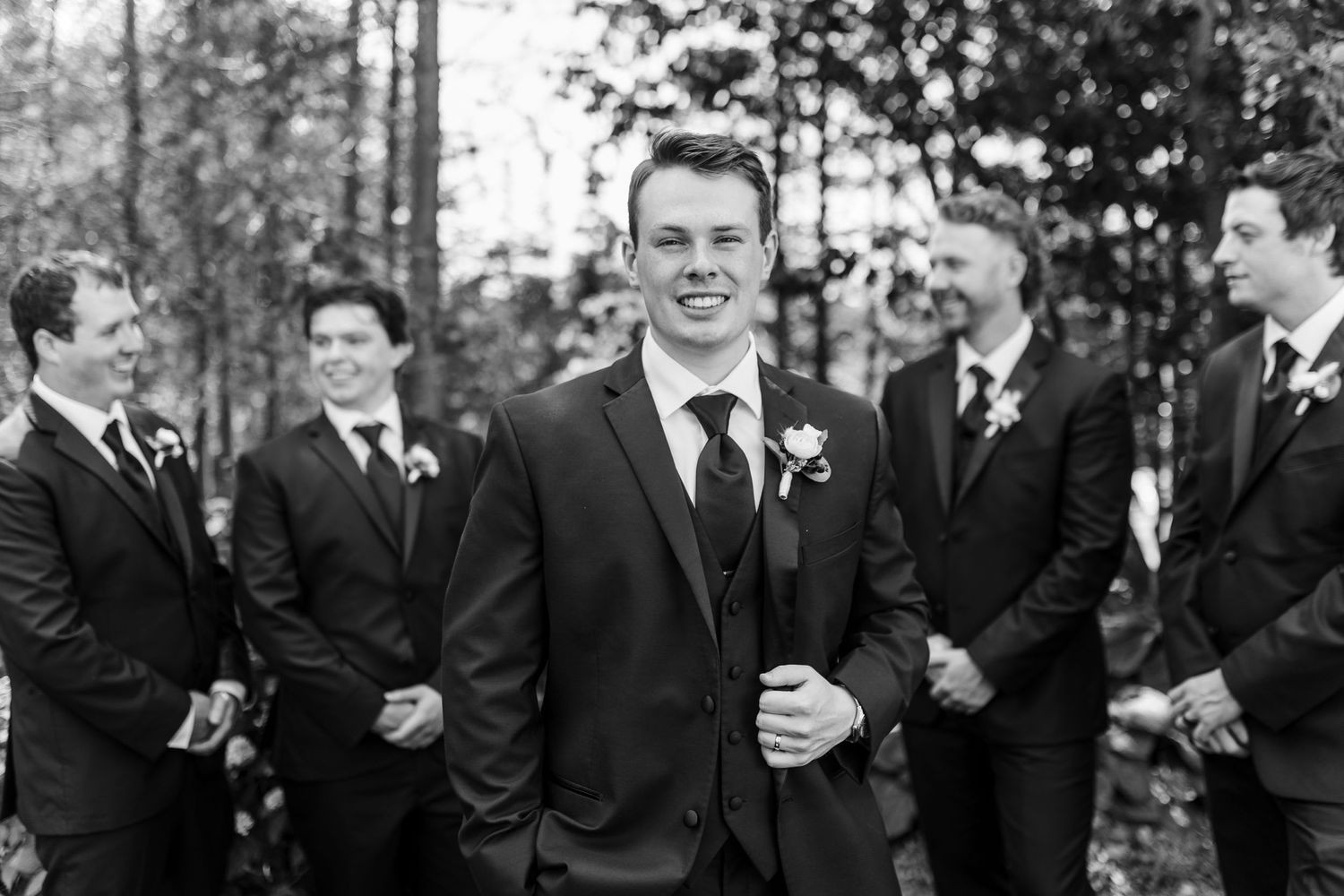 Black and white portrait of wedding party members sharing candid moment outdoors.