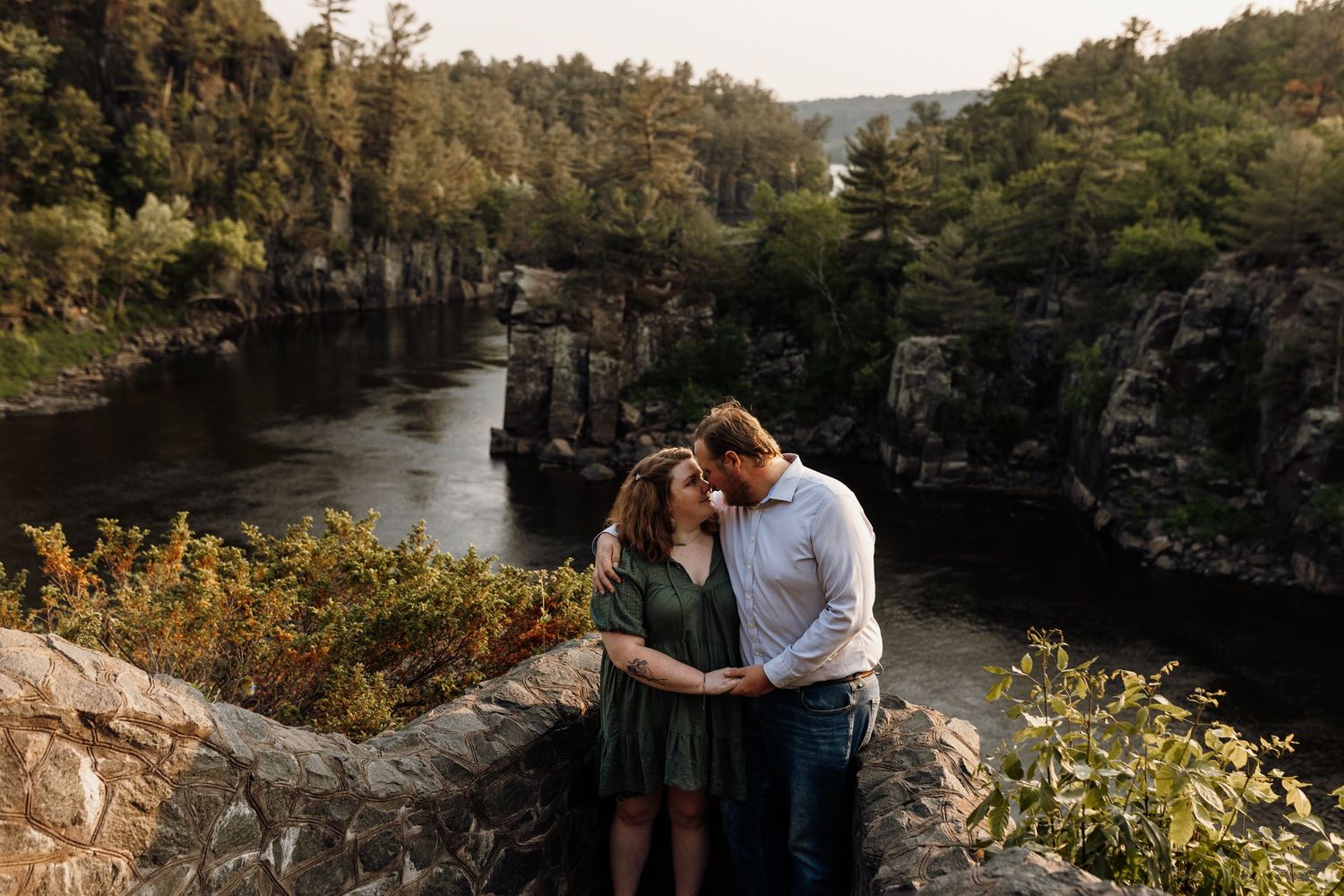 A couple sharing an intimate moment at a scenic overlook with dramatic cliffs and river below.