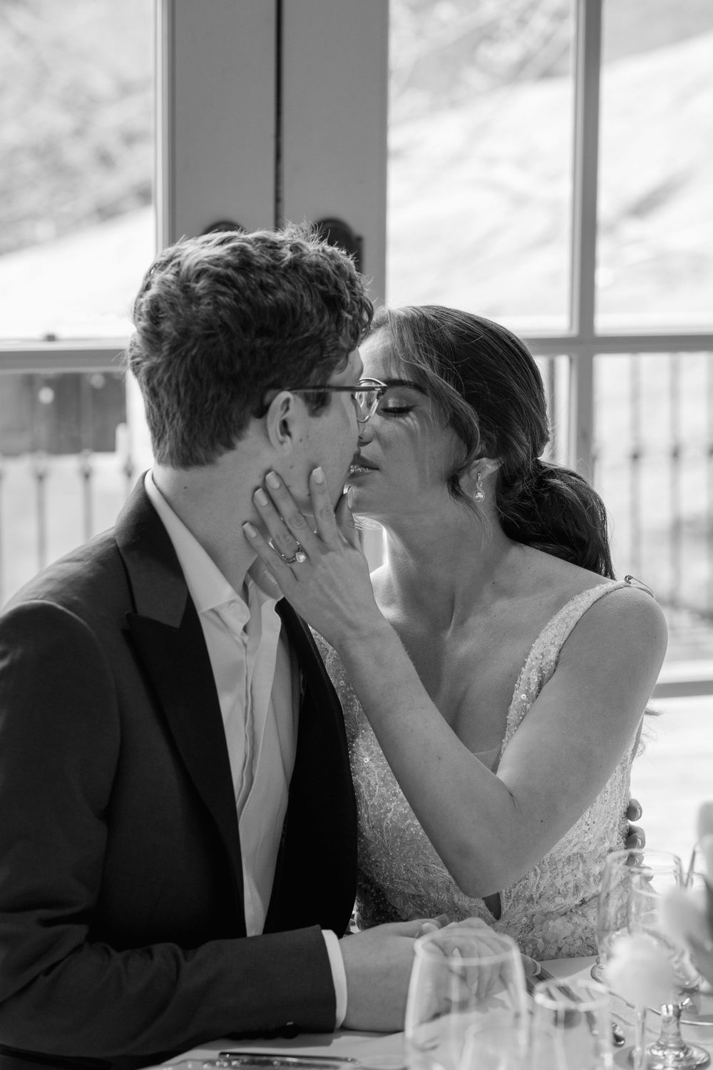 Intimate black and white photo of newlyweds sharing a tender moment at their reception table.