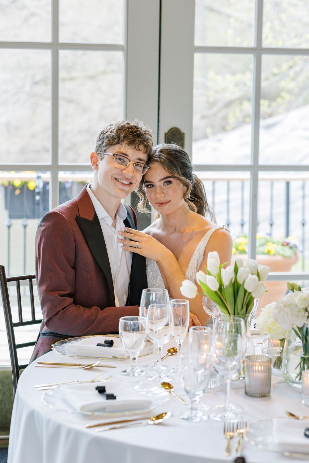 Wedding couple poses at elegant table setting with white tulips and glassware.
