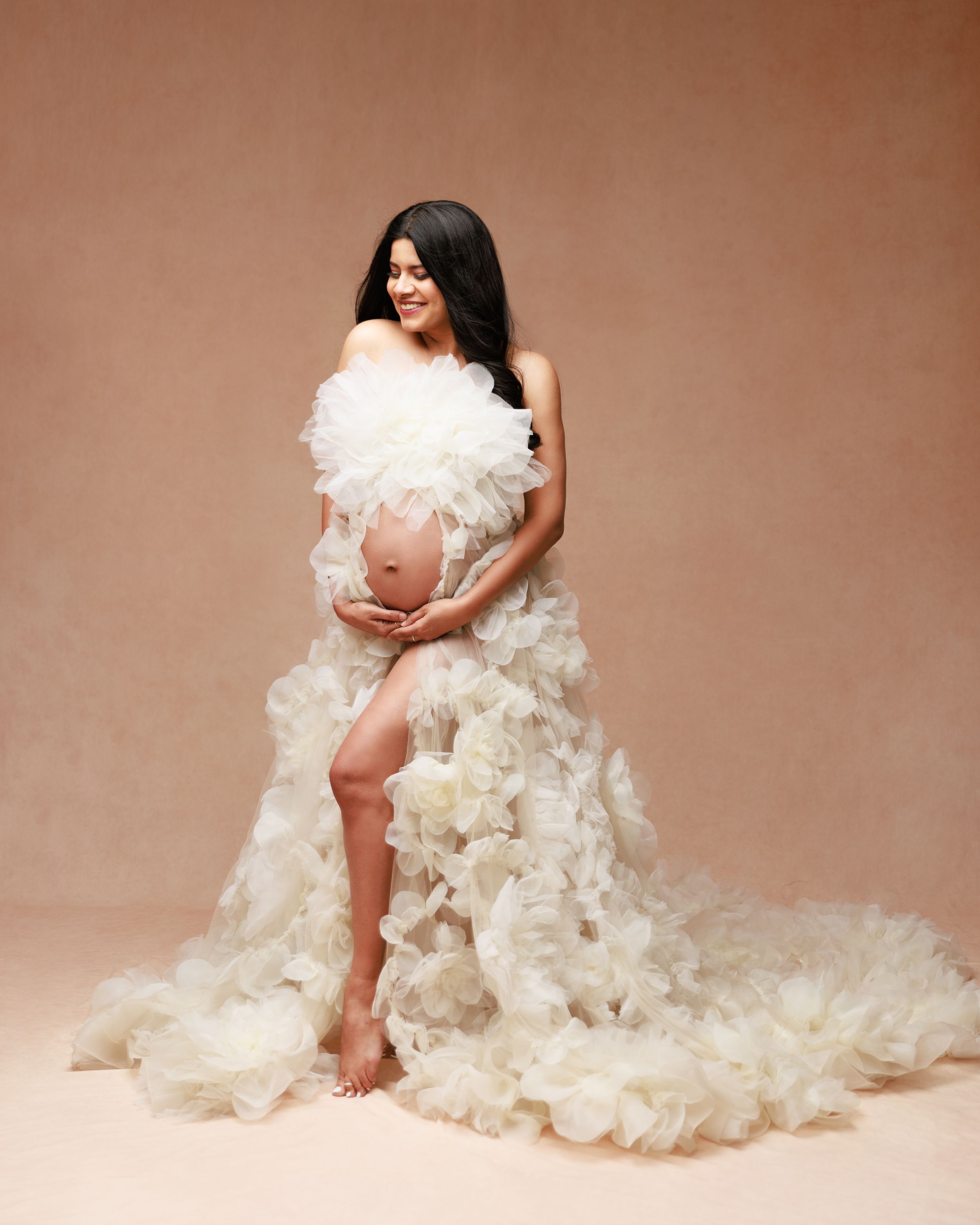 Dreamy maternity photo with cascading white tulle fabric against neutral background.