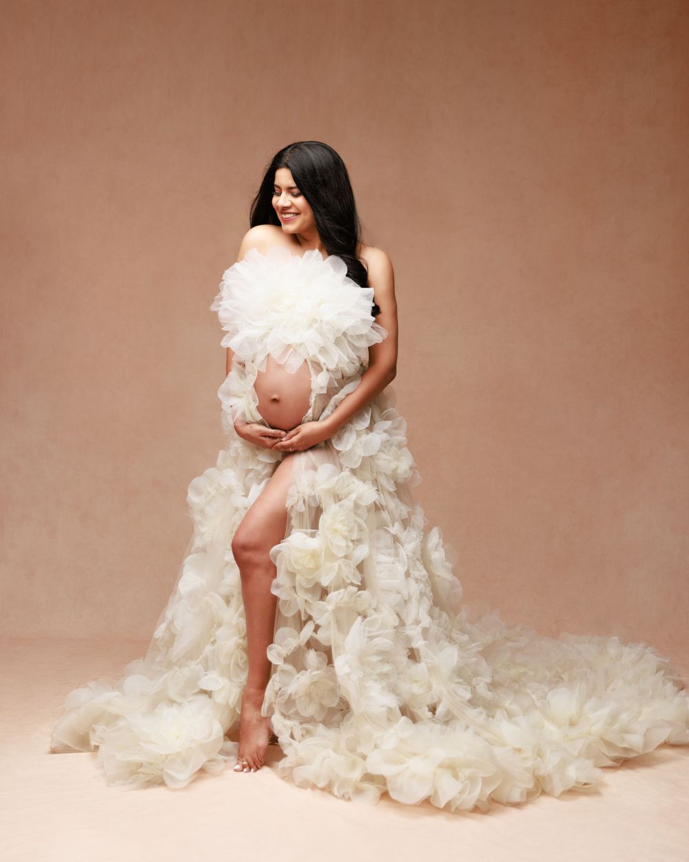 Dreamy maternity photo with cascading white tulle fabric against neutral background.