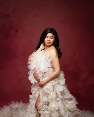 Studio maternity portrait featuring elaborate white tulle gown against deep red background.