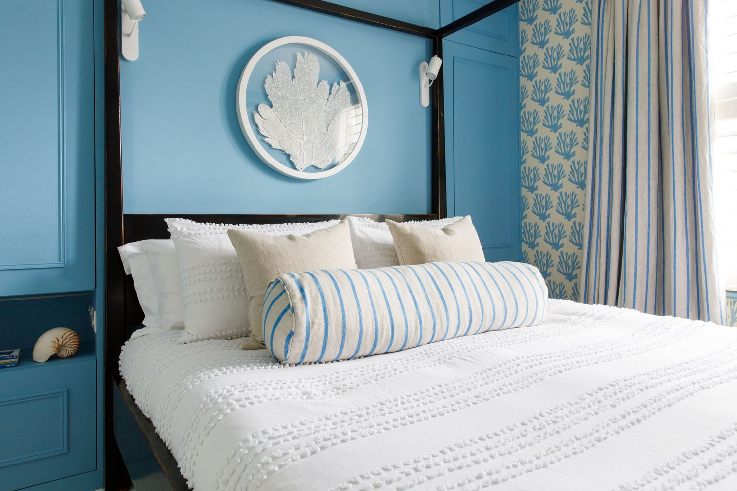 Blue bedroom with white bedding, striped pillows, and decorative wall clock.