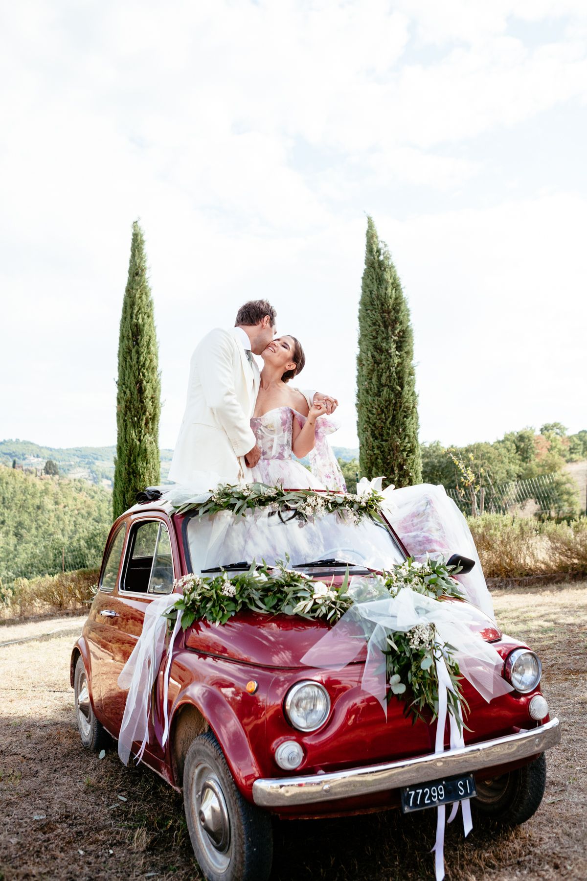 groom kisses a smiling bride as they stand in a fiat 500 at their destination wedding in Italy