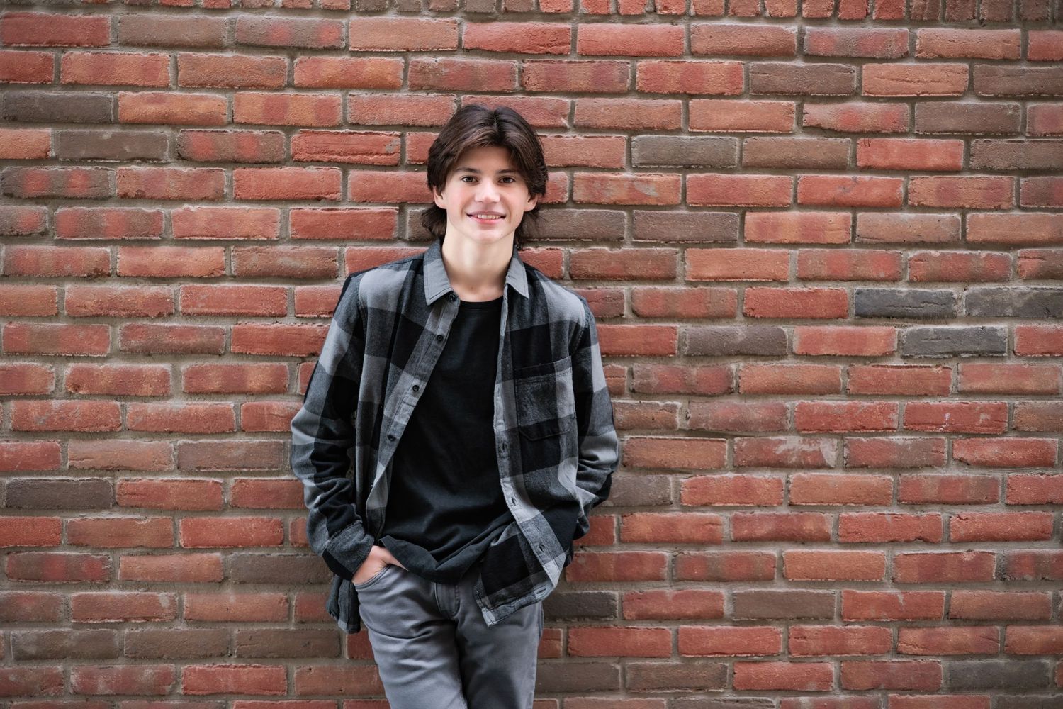 Casual portrait against red brick wall wearing plaid shirt and jeans.