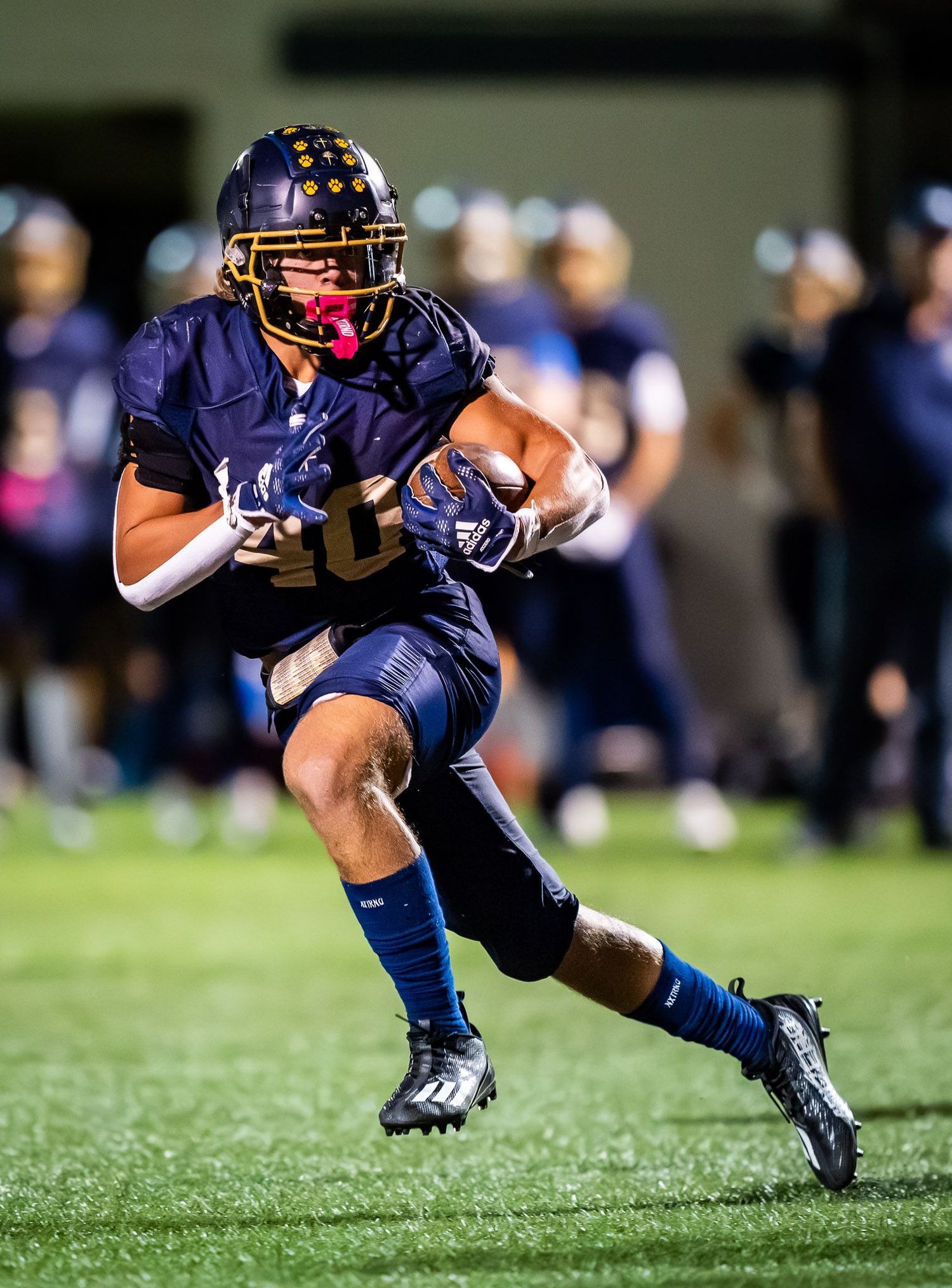 Football player in navy uniform carrying ball during night game with intense focus and determination.