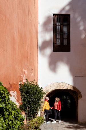 Two people standing beneath arched doorway against coral and white walls.