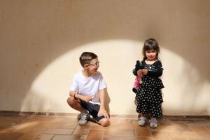 Two children sitting against a wall in sunlight and shadow.