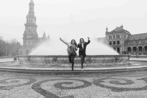 Two joyful silhouettes leaping in front of a fountain in a historic European plaza.